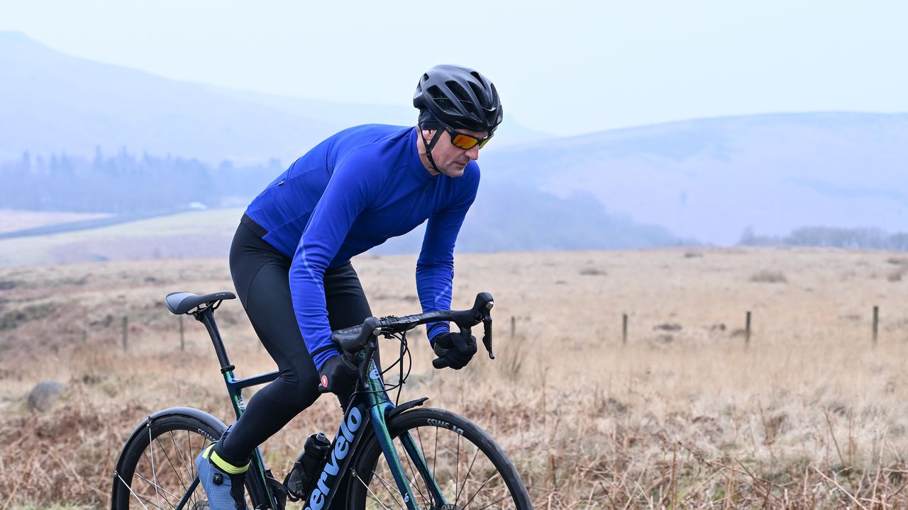 Man riding a bike out of the saddle wearing a blue Madison DTE Isoler Jacket