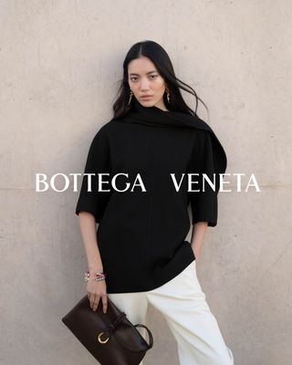 A model in a black Bottega Veneta sweater, white pants, and brown Liberta bag