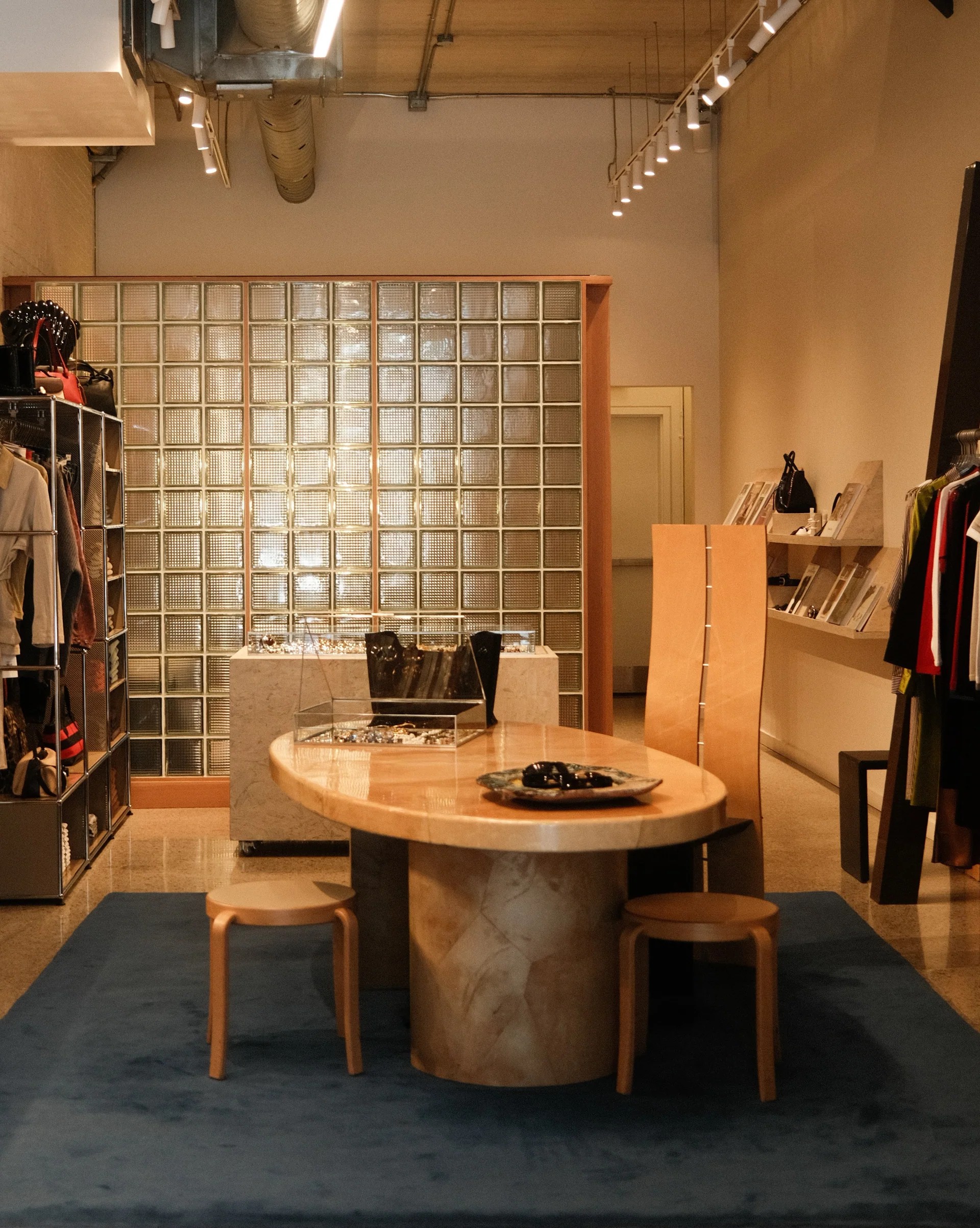 A beautifully curated fashion and design showroom, with glass blocks, sculptural furnishings, and a pale yellow and chrome aesthetic.