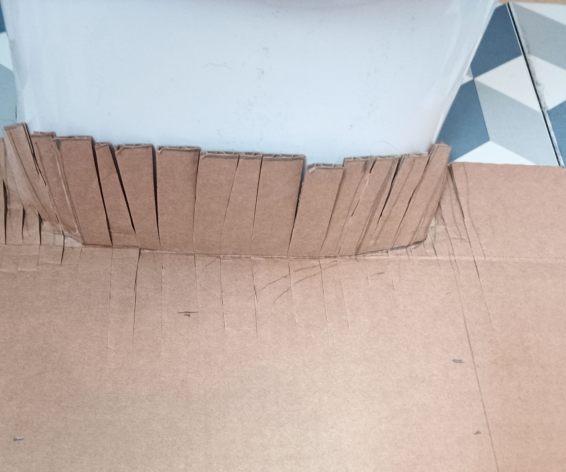 Cardboard template on the floor up against base of the toilet with cuts to mark the curve