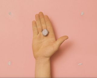 A person holding adhesive blu tack to remove blu tack on walls