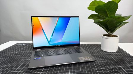 The Asus Vivobook 16 Flip convertible laptop on a black and white desk, against a gray background.