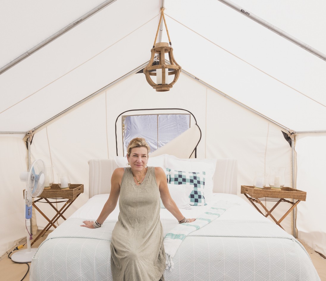 A relaxed older woman sits on a king-size bed in a glamping tent.