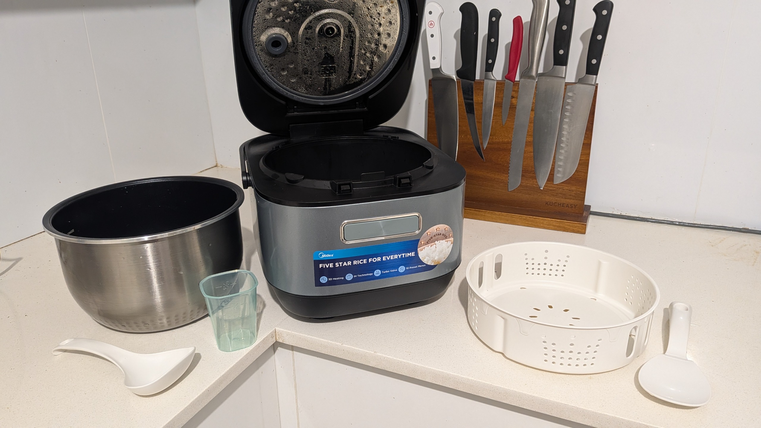 Midea 5L Induction Rice Cooker and its accessories laid out on a kitchen countertop