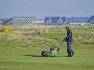 A greenkeeper uses a hand mower to cut a green in preparation for The Open
