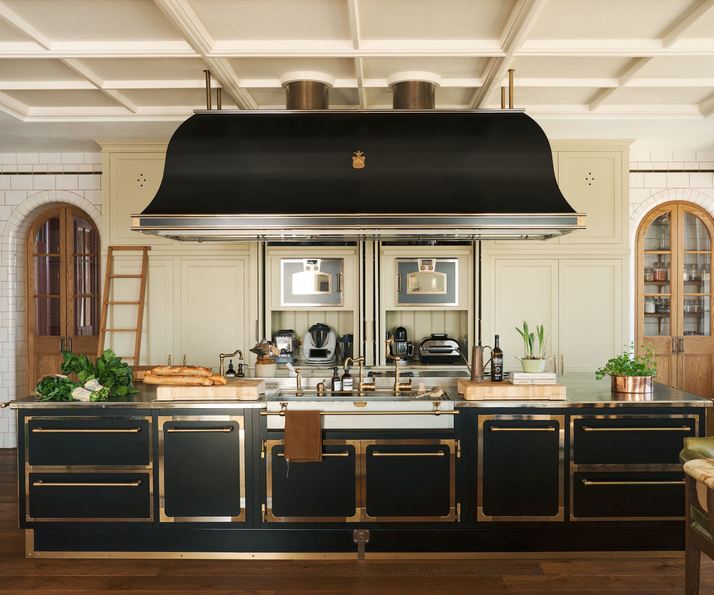 A cream and black kitchen with an oversized range hood above the island and cutout details on the wall to floor cabinets