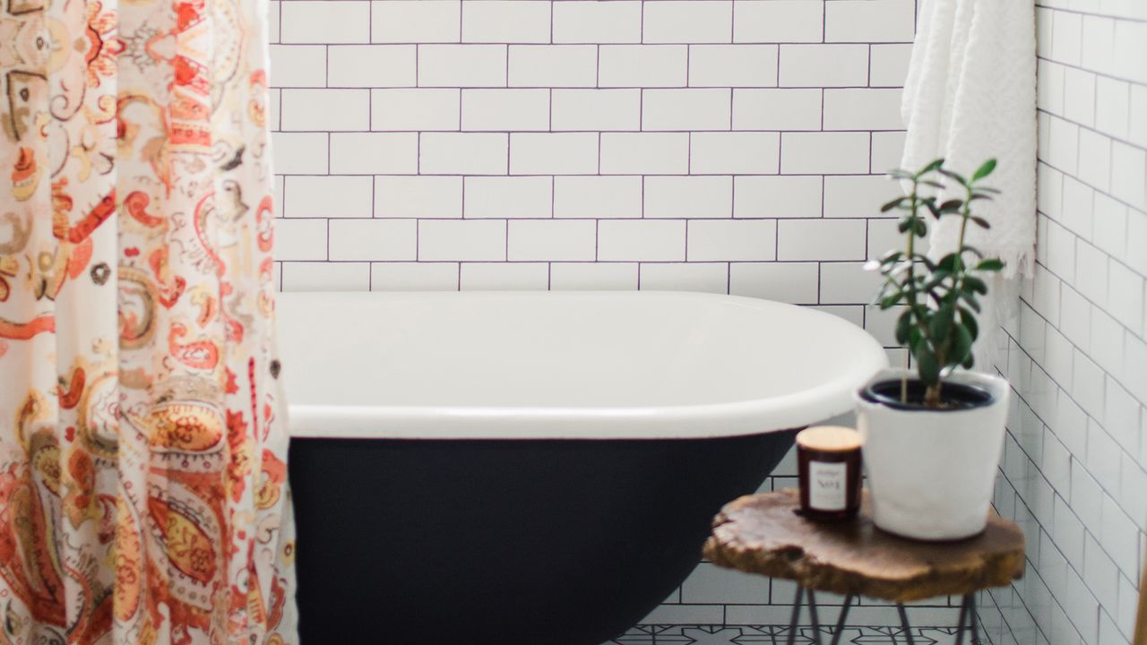 bathroom subway tiles with black grout, black freestanding bath and orange patterned curtain 