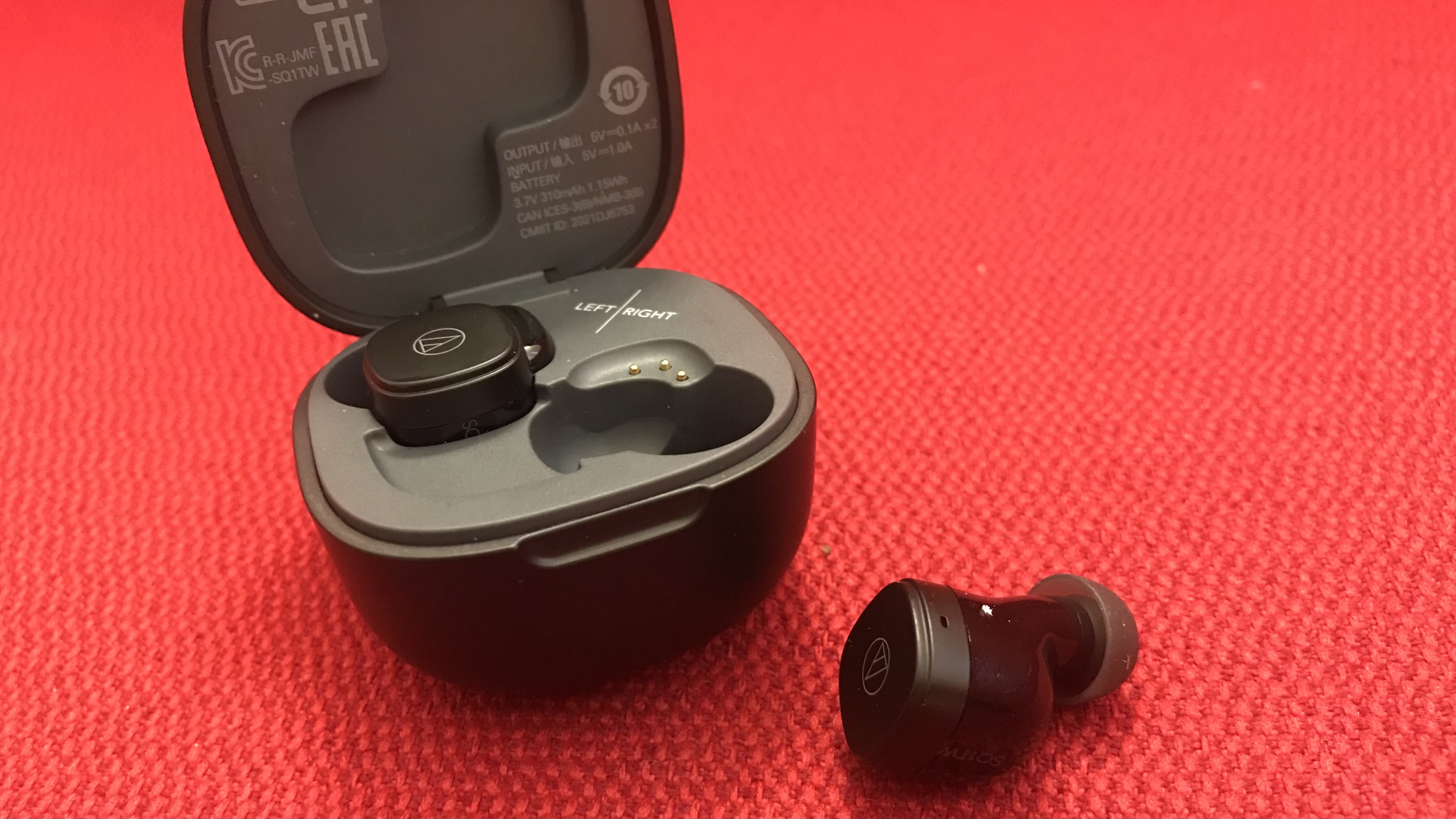Audio-Technica ATH-SQ1TW earbuds out of case, on red background