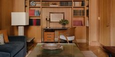 timber clad room with built-in desk and bookshelf, navy sofa, glass coffee table, and large white floor lamp