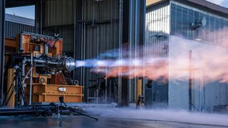 a horizontally placed rocket engine blasts out blue-orange exhaust during a static-fire test.
