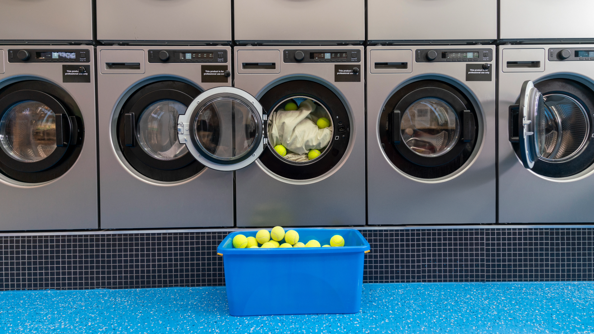 A box of tennis balls in front of lots of washing machines and one with tennis balls inside
