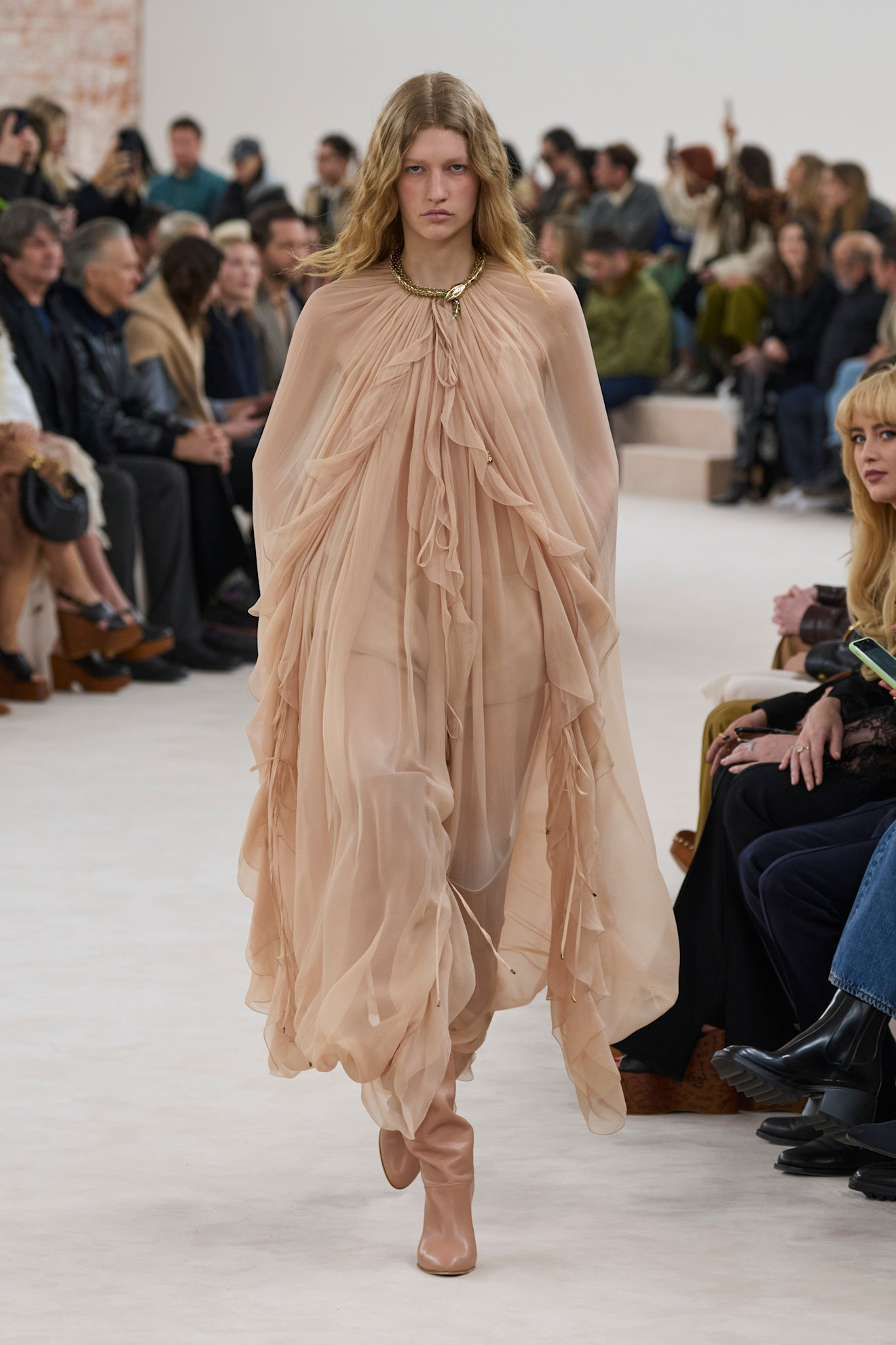The Chloe Autumn Winter 2024, Ready to Wear runways show. The model wears a draped maxi dress and knee high boots. This image was taken from Launchmetrics.