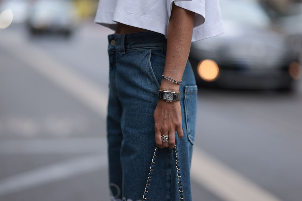 Kathrin Bommann wearing silver Celine sunnies, silver Tiffany City Hardware collection necklace, white Vival Studio cropped t-shirt, wide leg blue Loewe jeans with white logo patches, silver Cartier tank watch, denim Chanel Classic Flap Bag and white Hermes Chypre sandals on July 13, 2023 in Dusseldorf, Germany.