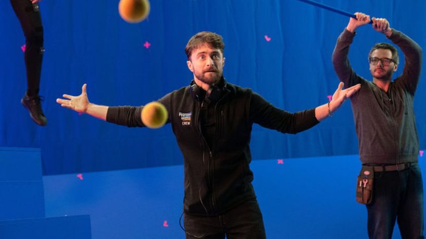 Daniel Radcliffe standing in front of a blue screen around tennis balls looking upset and distraught. 