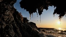 the sun sets behind icicles melting on permafrost in Alaska with a river in the background