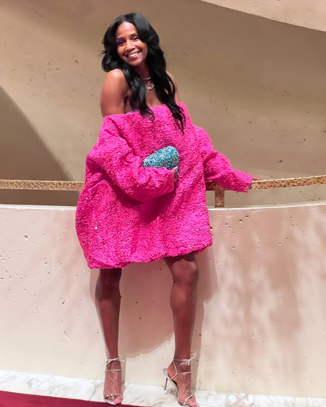A woman with black hair wearing a pink dress and silver strappy heels