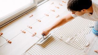 Man spreading tile adhesive with a notched trowel onto wooden floor with cement backer board 