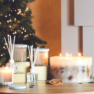 Collection of candles displayed on tabletop with Christmas tree in background