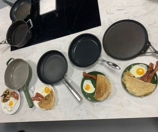 A line of frying pans next to plates of cooked breakfasts.