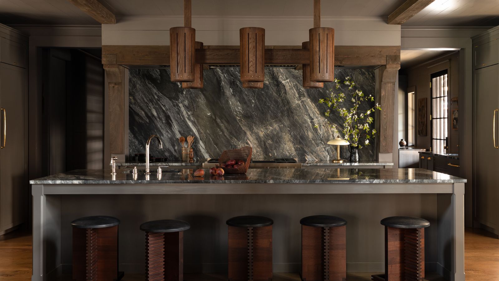 Open-plan farmhouse kitchen with a large marble island, dark marble backsplash, reclaimed wood beams, and vintage wooden stools.