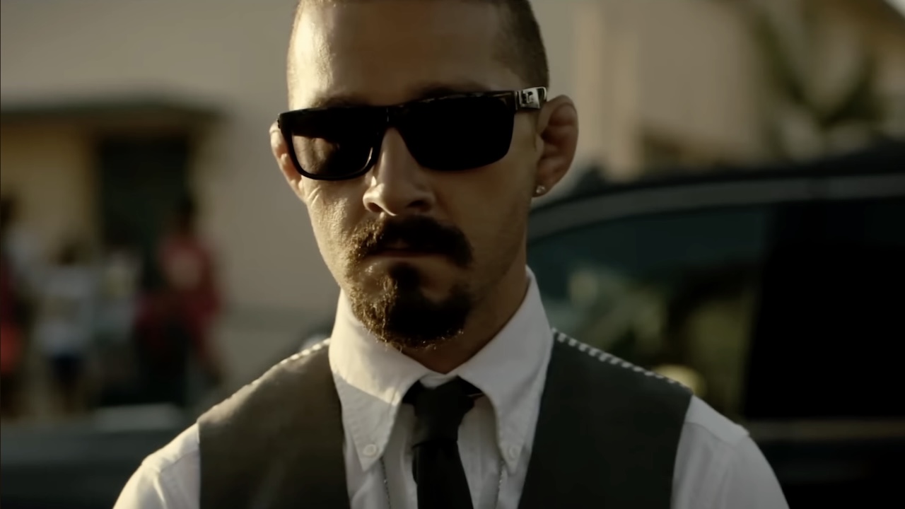 Shia LaBeouf wearing sunglasses, white collared shirt, tie and vest in The Tax Collector