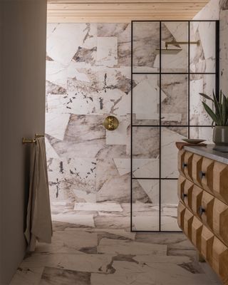 A shower room with floor to ceiling marble effect tiles and a glass shower enclosure