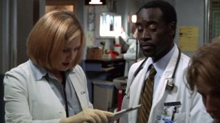 Don Cheadle wearing a doctor's coat, looking down at something in ER