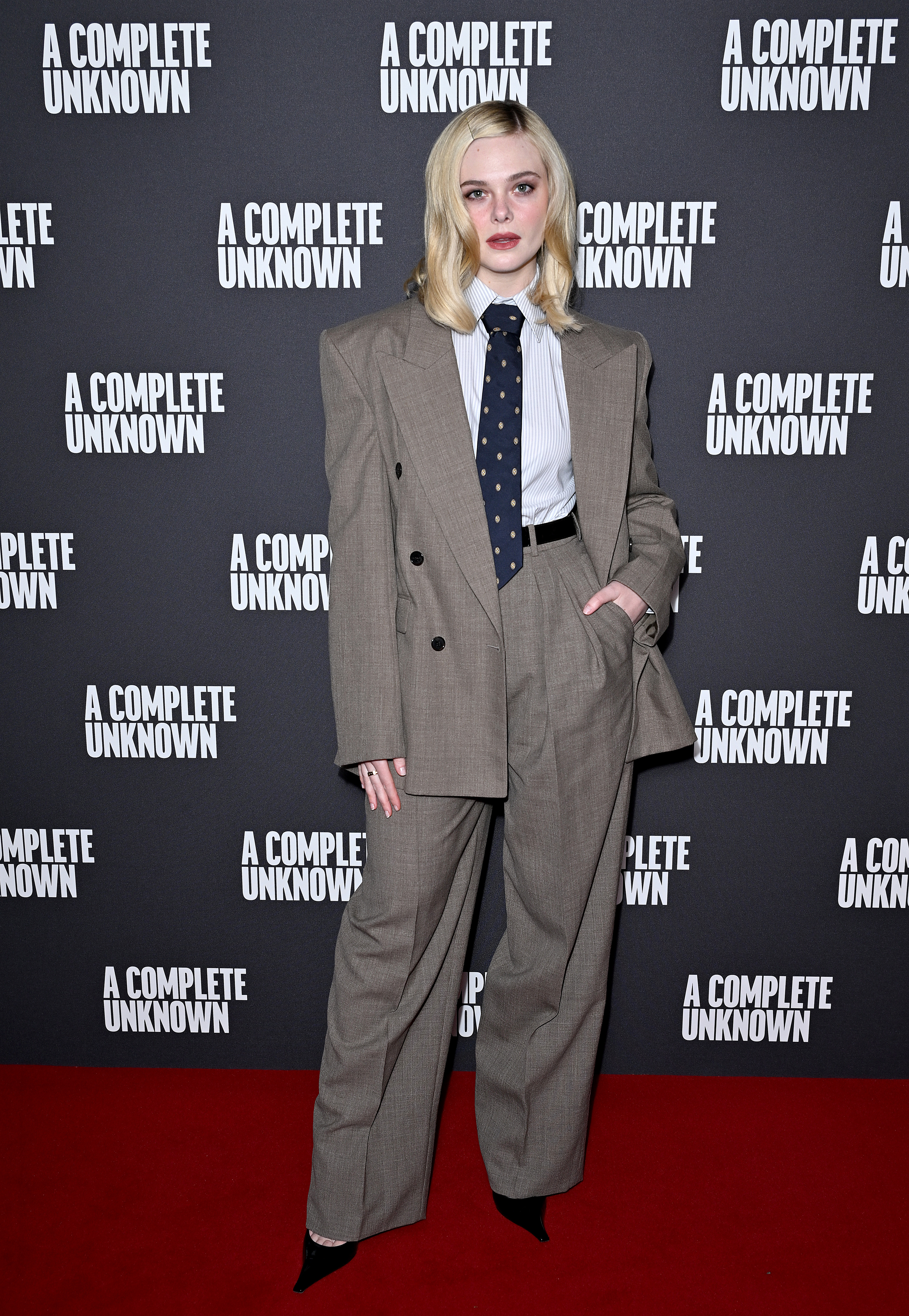 Elle Fanning wearing a gray suit, blue shirt, and blue necktie at the UK photocall of "A Complete Unknown" on December 16, 2024 in London, England. (Photo by Kate Green/Getty Images for The Walt Disney Company Limited)