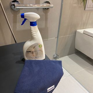 Shower cleaning bottle and cloth on grey worktop next to shower screen