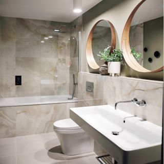 bathroom with beige tiles, green plant, white basin and 2 wooden mirrors