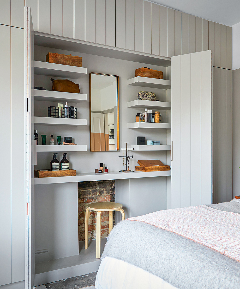Gray built-in cabinetry housing a dressing table, mirror and shelving.