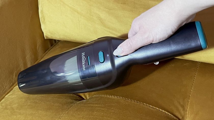 A woman is vacuuming a mustard colored sofa with the Homekane Handheld Vacuum.