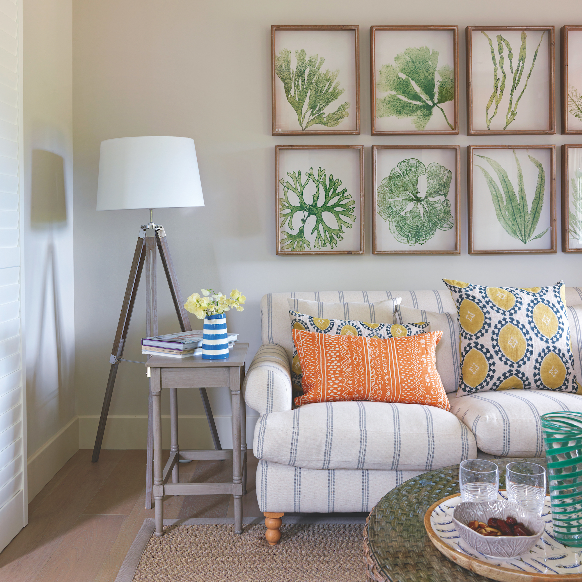 living room with white sofa with blue stripes and colourful orange and yellow cushions with green seaweed artwork on wall