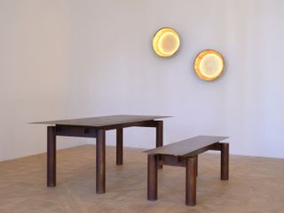 Exhibition installation view with a table and wall lights