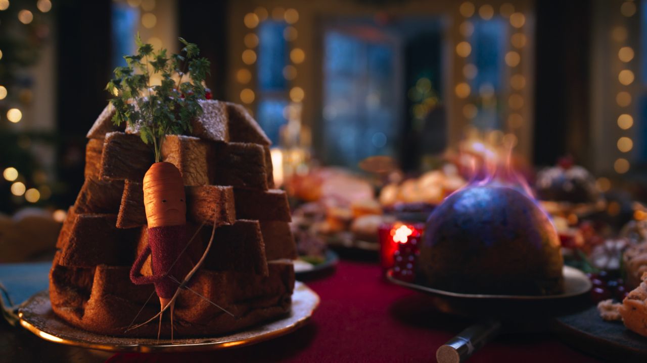 Aldi&#039;s Kevin the Carrot hiding behind a table filled with food