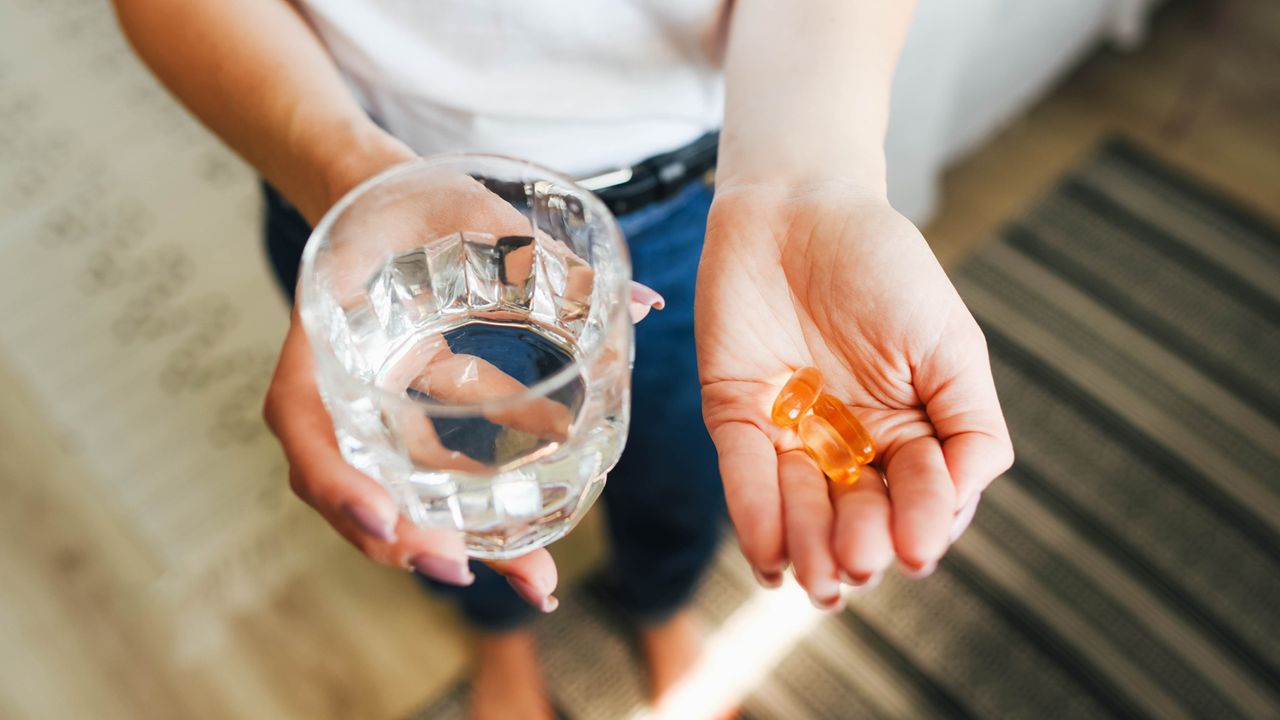 Woman holds magnesium tablets in one hand and a glass of water in the other