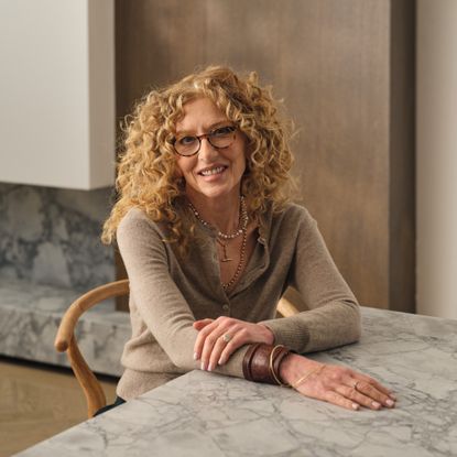 A portrait of Kelly Hoppen sitting at a marble dining table