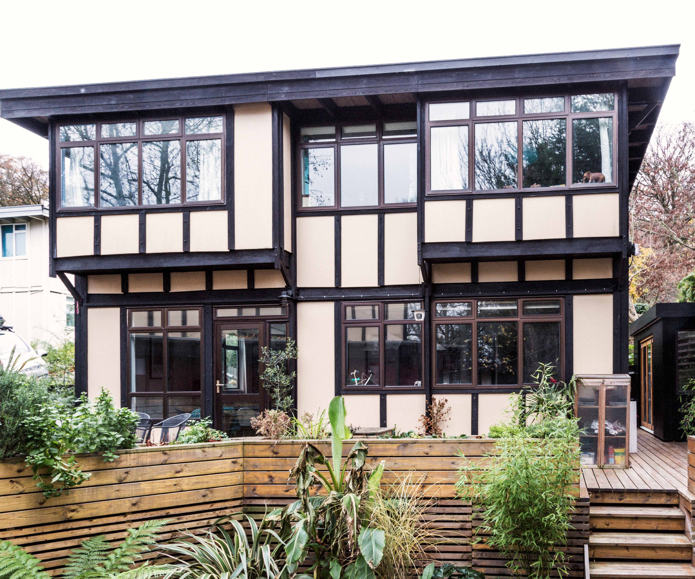 before shot of exterior of timber framed house with cream panels and wooden framed windows leading to garden and patio