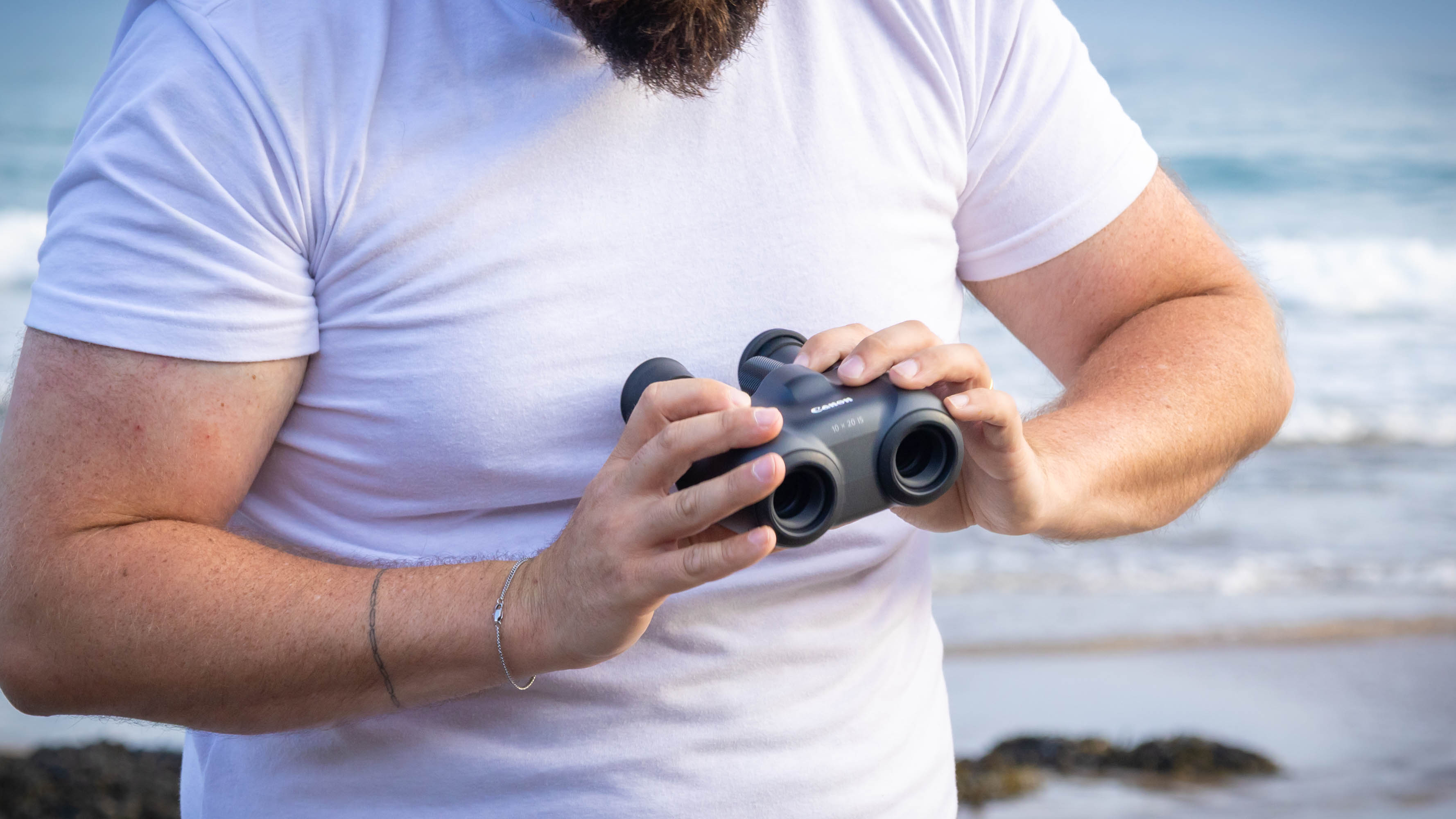 A person holding the Canon 10x20 IS binoculars, showing the objective lenses.