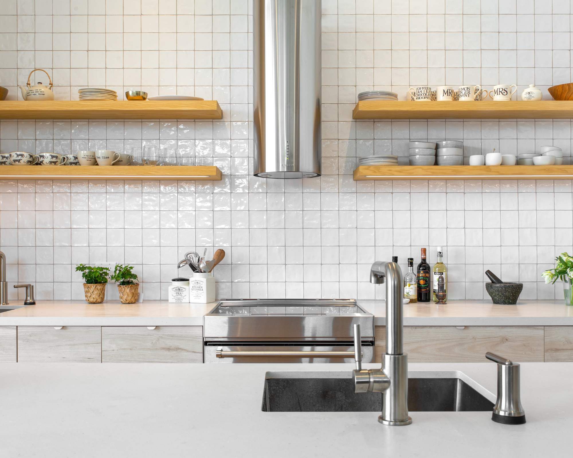 White tile Scandinavian kitchen design with light wood open shelving, and island with chrome faucet and curated finish