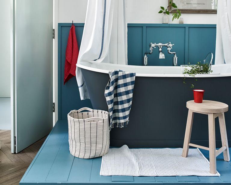 An example of small bathroom storage ideas showing a dark blue freestanding bath next to a basket and a wooden stool