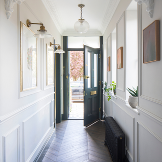 White hallway with paneling on the walls and herringbone flooring, leading to a blue front door