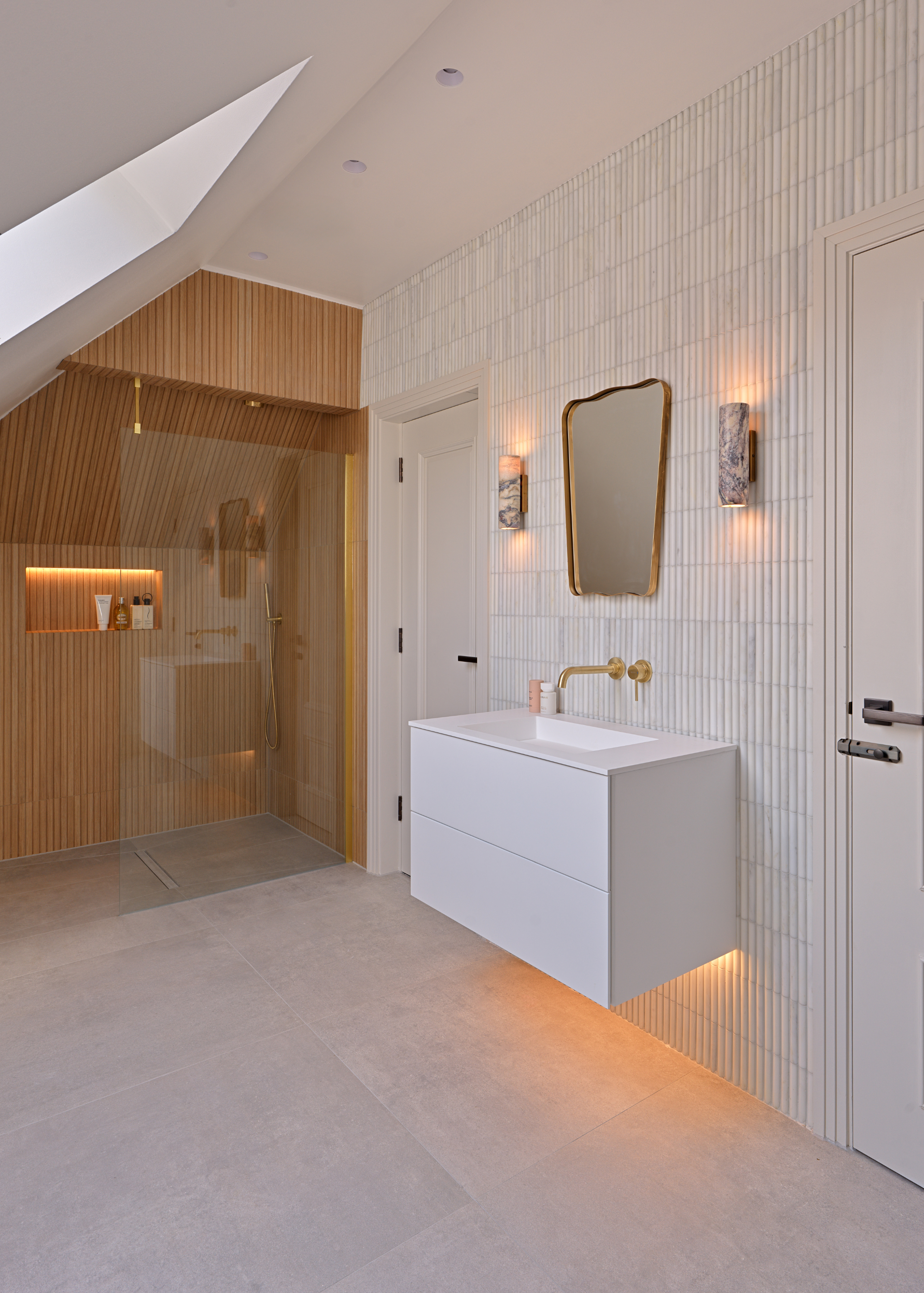A spa-like bathroom in a neutral and white palette with brushed brass fixtures and fittings and a wooden effect area where the shower is positioned