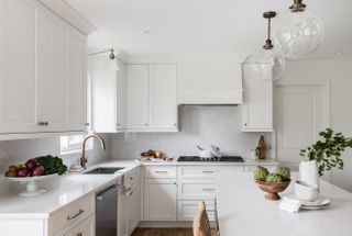 A white kitchen with white cabinets, a large island, and glass globe pendants and a glass wall light, both with brass hardware