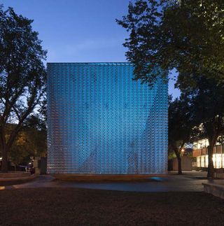Textured metal cube lit from within at dusk in a public garden