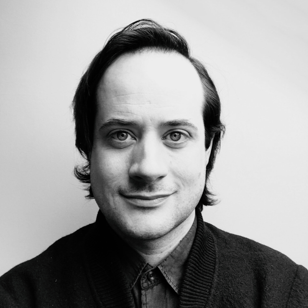 black and white image of male with short dark hair wearing dark jacket and shirt