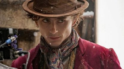 Timothée Chalamet as Wonka in the Wonka movie, wearing a brown hat and a red coat.