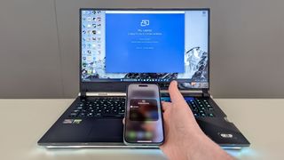 iPhone 16 in hand being held in front of Asus ROG Strix 17 on table showing screen mirroring not working