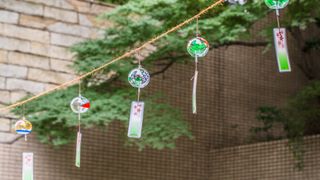 japanese wind chimes hanging from string in garden with brick wall and overhanging trees