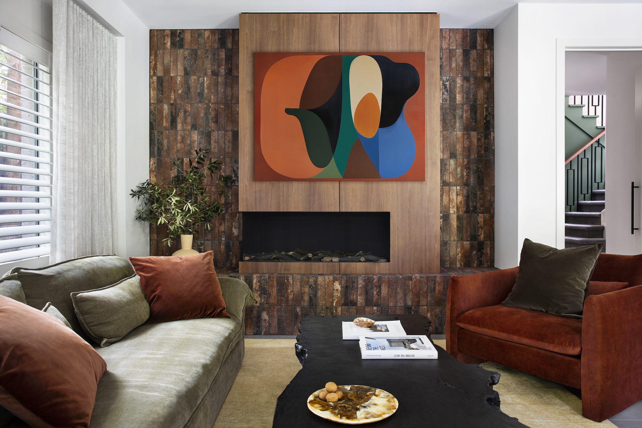 A modern living room with velvet sofas in red and sage green sat in front of a sleek brown fireplace of wood and brown tiles